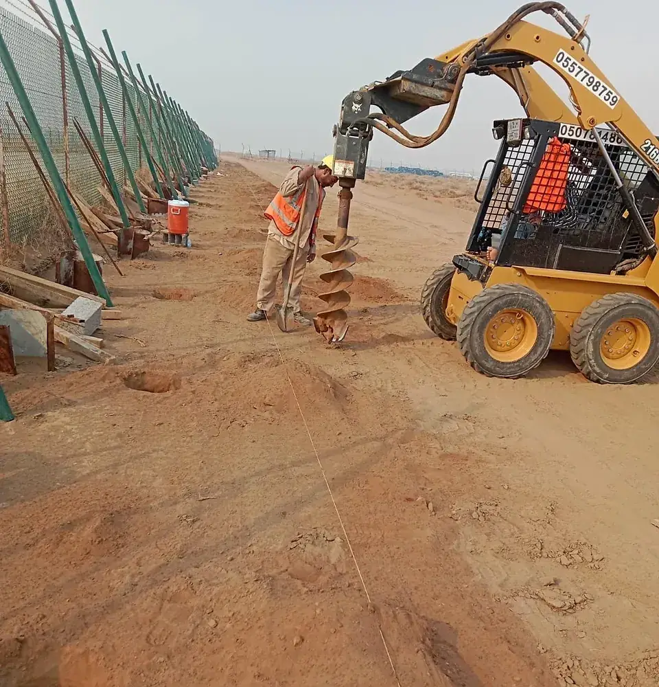 Skid-steer auger drilling post holes for the fence line